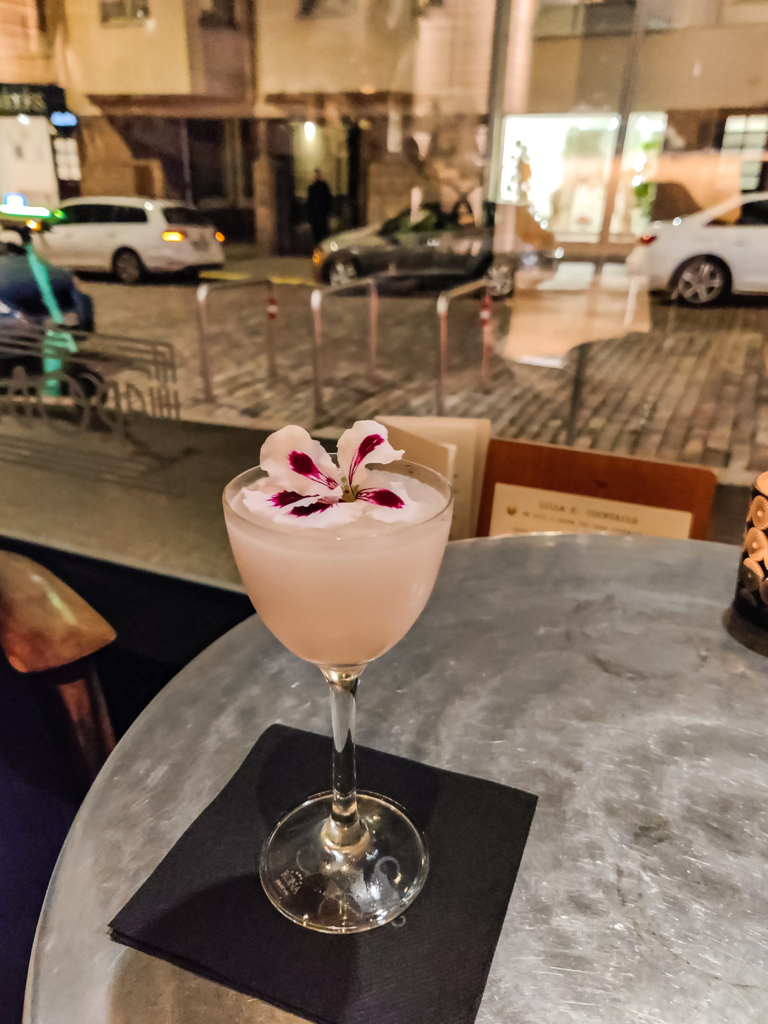 Jalallinen lasi, jossa on hennon vaaleanpunainen juoma ja päällä kukka.