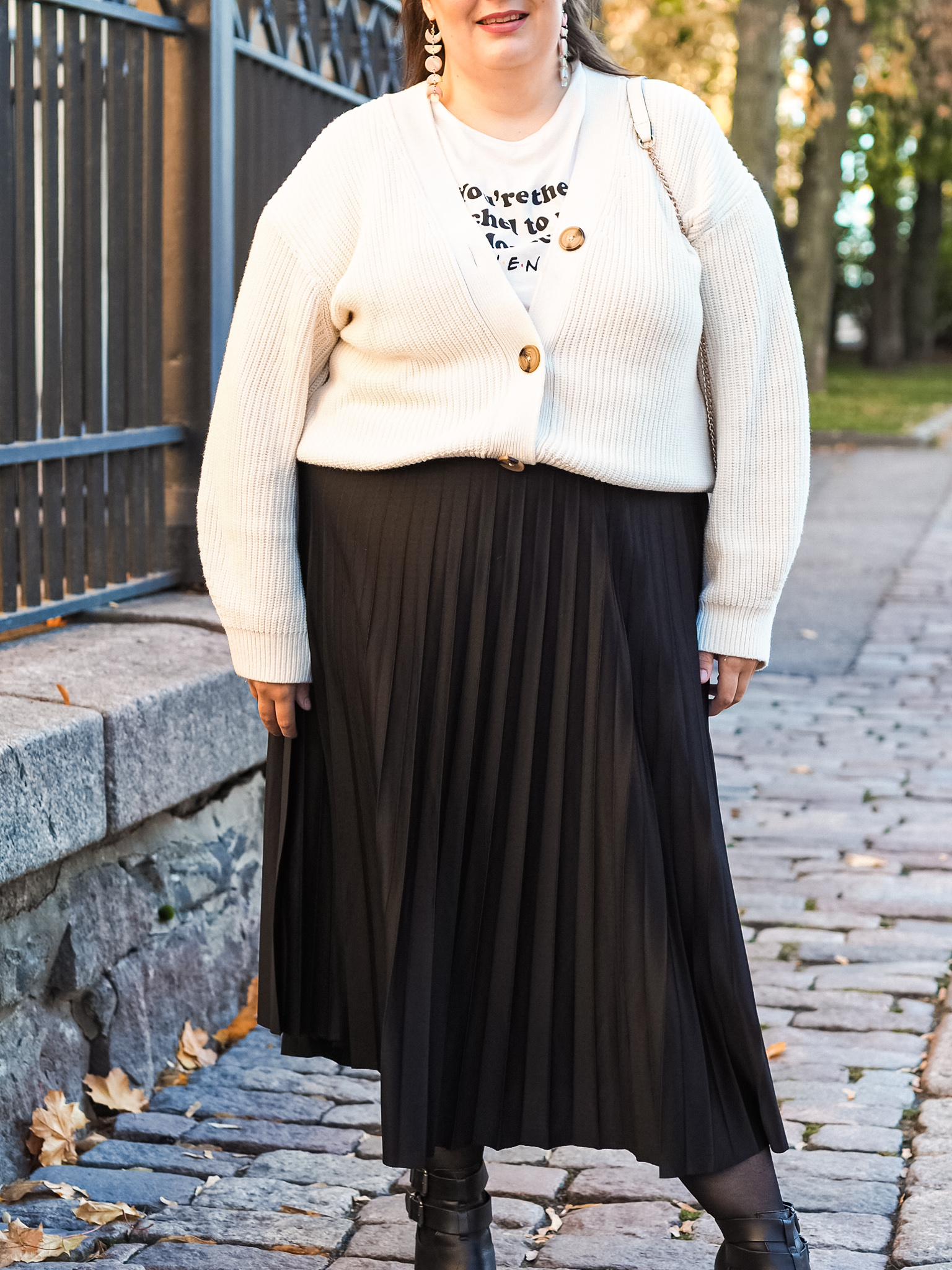 Naisella yllään neuletakki, sen alla valkoinen, tekstisomisteinen paita, sekä musta midimittainen vekkihame.