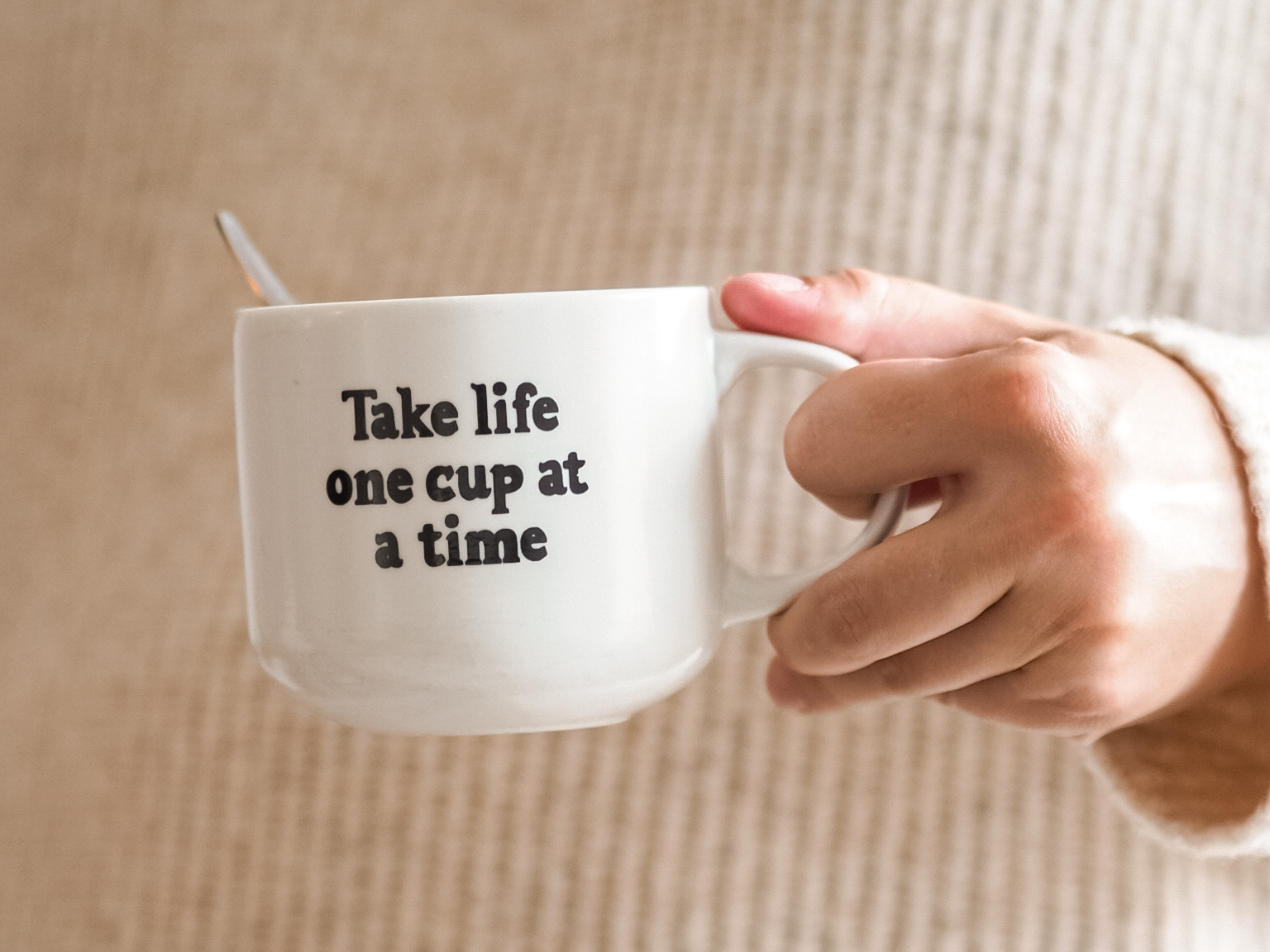 Käsi, joka pitelee kahvikuppia, jossa lukee: Take life one cup at a time.